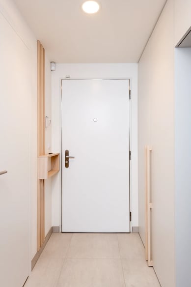 Bílý interiér chodby s dveřmi a dřevěným detailem.